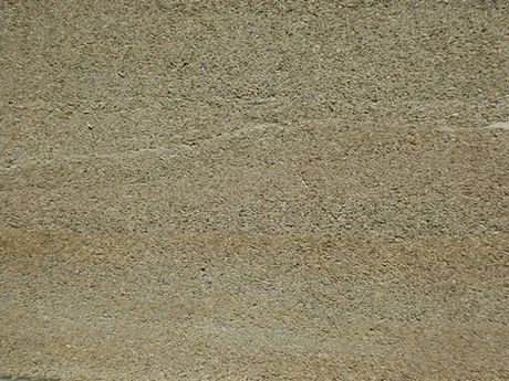 A close-up view of a rough, textured beige hempcrete wall surface, showing subtle horizontal lines and variations in colour and texture.