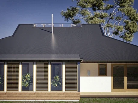 Modern house with a dark sloped metal roof, large windows with wooden shutters, and a light timber exterior. Designed as a breathable home, it sits beneath a clear blue sky with a tall tree partially visible behind the house.